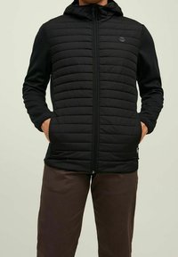 Chaqueta acolchada negra con capucha, presenta un diseño acolchado en el cuerpo, mangas lisas, bolsillos laterales y cierre frontal con cremallera.