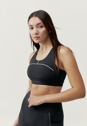 Sort sports-bh med et sømløst design, der har en grå accentlinje over brystet og en glat overflade. Justerbare stropper og bånd.