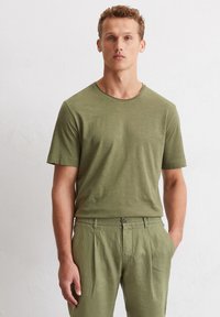 Olivgrünes T-Shirt mit kurzen Ärmeln und rundem Halsausschnitt, aus leichtem Stoff und mit lockerer Passform, kombiniert mit passenden grünen Hosen.