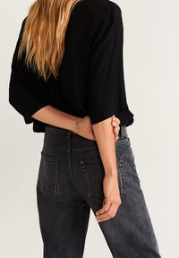 Schwarzes, lässig geschnittenes Oberteil, hochgeschnittene, dunkelgraue Jeans mit Gesäßtaschen, von hinten betrachtet, wobei der Stoff und die Passform hervorgehoben werden.