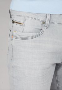 Jeans in denim grigio chiaro con vestibilità slim, dotati di cuciture a contrasto, una tasca con zip e tasche frontali e posteriori standard.