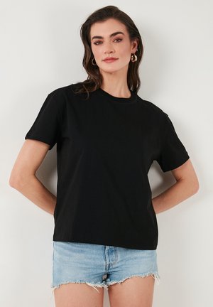 Zwarte katoenen t-shirt met korte mouwen en een ronde hals, gecombineerd met lichtblauwe denimshorts met rafelige zoomdetails.