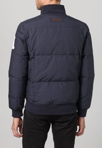 Navy padded jacket with a high collar, ribbed cuffs, and a logo patch on the back. Features quilted texture and lightweight material.