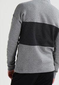 Šedá mikina s černým horizontálním pruhem uprostřed, vyrobená z měkké bavlněné směsi s žebrovanými manžetami a hladkou texturou.