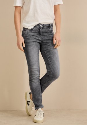 Los pantalones vaqueros gris denim tienen un corte ajustado con una cintura de altura media. La textura es suave, con un acabado desgastado. Se combinan con zapatillas blancas y una camisa clara.