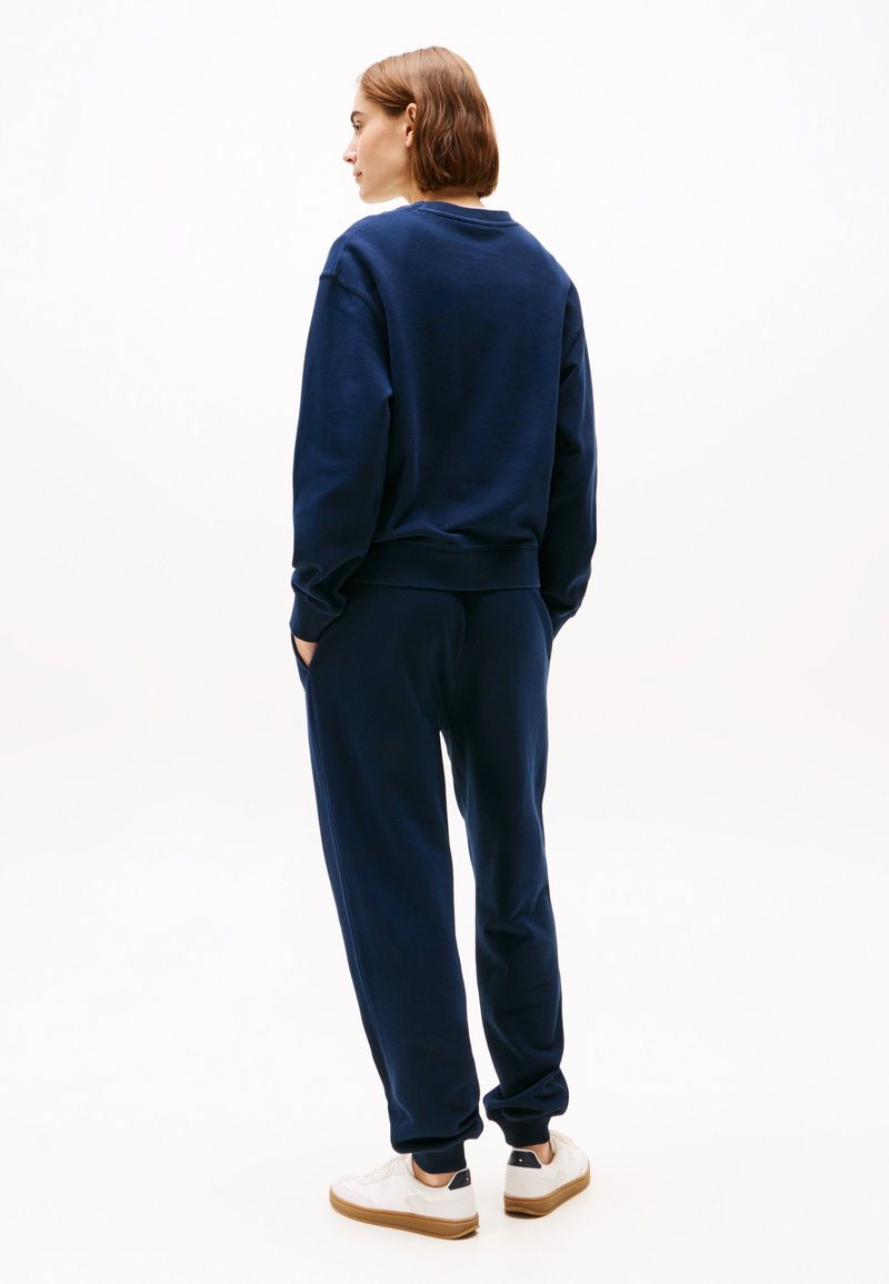 Marineblauwe sweatshirt en bijpassende joggers van zacht materiaal. De outfit heeft een casual pasvorm en ribgebreide manchetten, gecombineerd met witte sneakers.