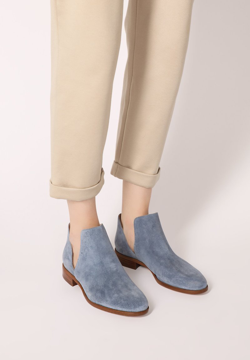 Helle blauene Wildleder-Stiefeletten mit niedrigem Absatz und seitlichen Ausschnitten werden mit beigen, umgeschlagenen Hosen kombiniert. Sanfte Textur und elegantes Design.