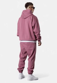 Sweatshirt rose surdimensionné avec capuche, associé à un jogging assorti. Présente des poignets côtelés et des baskets blanches pour un look harmonieux.