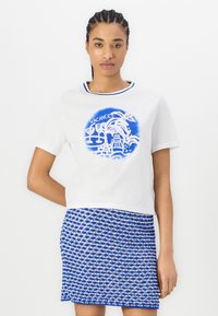 Hvid kortærmet t-shirt med blåt grafikdesign med palmer og drikkevarer, parret med en blå og hvid mønstret nederdel.