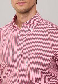 Rot-weißer gestreifter Button-up-Hemd mit Kentkragen, kleiner Tasche und glatter Baumwollstruktur. Bemerkenswerte Stickerei auf der Tasche.