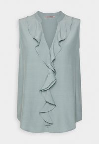 Blouse sans manches bleu clair avec un décolleté en V, arborant un volant prononcé au centre. Tissu lisse avec une texture douce.