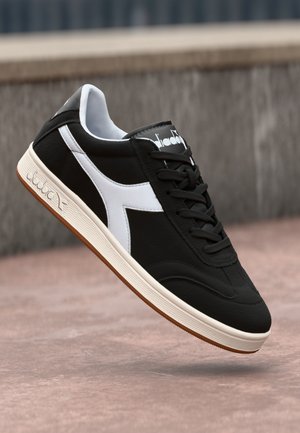 Baskets en cuir noir avec des accents blancs, surface texturée, design à lacets et semelle en caoutchouc beige. Logo visible sur le dessus.