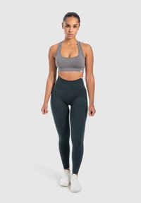 Grijze sportbeha met een ronde halslijn, gecombineerd met hoge, donkergroene leggings, beide in een soepel rekbaar materiaal, gedragen met witte sneakers.