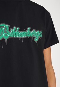 Czarna bawełniana koszulka z krótkim rękawem, z dużym, zielonym logo z kapiącym efektem i srebrnymi akcentami, na którym widnieje napis "Bikkembergs". Okrągły dekolt.