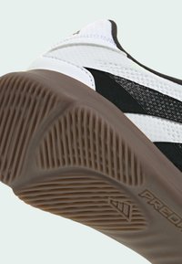 Zool van witte sneaker met bruine textuurgrip en zwart gestreepte details, die het profiel van de zool en een deel van de schoenbovenkant laat zien.