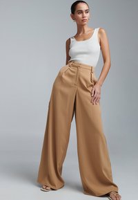 Beige vida byxor med hög midja och veck, kombinerade med ett vitt ribbat linne. Mjuk textur, elegant fall.