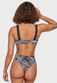 Bikini a rayas de cebra en blanco y negro con una parte inferior de cintura alta y tirantes gruesos, que presenta un detalle de cordones en la parte posterior.