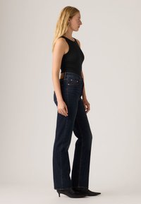 Μαύρο αμάνικο τοπ συνδυασμένο με σκούρο τζην καμπάνα. Το τζην έχει ψηλή μέση, ραφές σε χρώμα χαλκού και καφέ δερμάτινη ετικέτα στο πίσω μέρος.