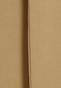 Tessuto beige con una texture a righe diagonali, caratterizzato da cuciture lisce. Il materiale appare resistente e di peso medio.