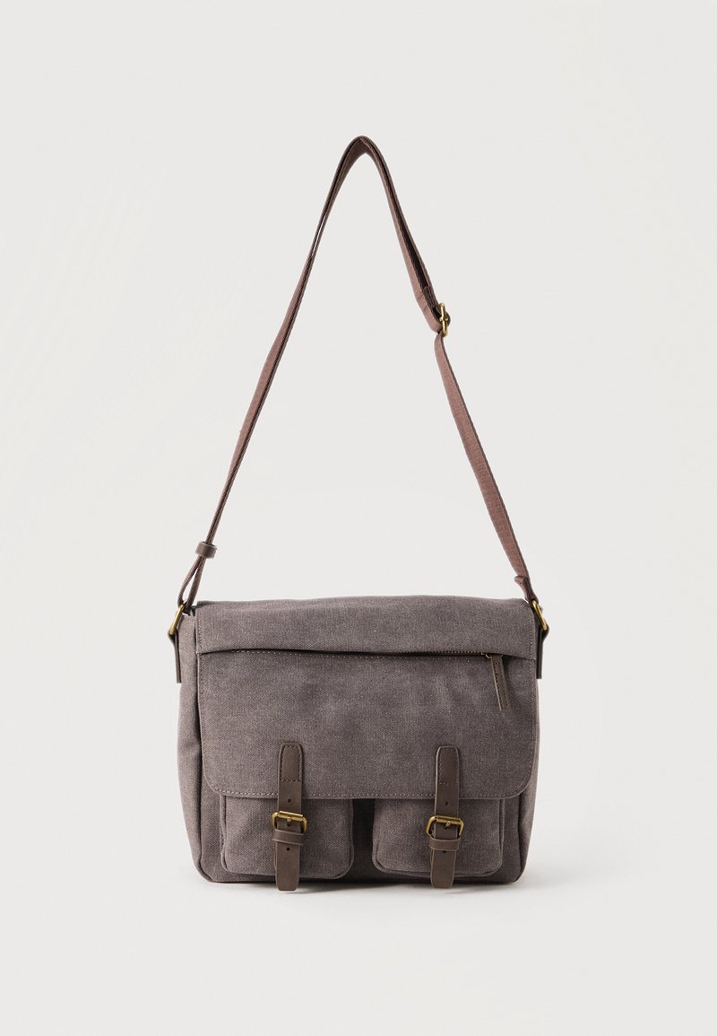 Γκρι καμβάς τσαντάκι ταχυδρόμου με ρυθμιζόμενο ιμάντα ώμου, εμπρόσθιο καπάκι με φερμουάρ και δύο τσέπες ασφαλισμένες με πόρπες.