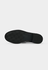 Semelle de chaussure habillée noire avec motif floral texturé et section de talon rainurée, photographiée sur un fond gris clair uni.