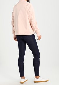 Giacca bomber rosa chiaro con maniche arricciate, abbinata a jeans skinny scuri e sneakers bianche. Tessuto liscio, design con vestibilità rilassata.