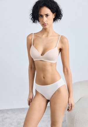 Nude-BH mit dünnen Trägern und tiefem Ausschnitt, kombiniert mit weißen, hoch geschnittenen Unterhosen. Glattes Material und minimalistisches Design.