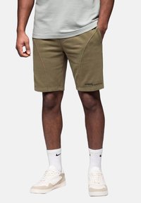 Shorts kaki en tissu doux, avec une coupe droite et des coutures latérales. Portés avec des chaussettes blanches et des baskets crème.