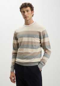 Maglione a righe beige e grigio realizzato in tessuto morbido, con collo a giro e polsini a coste. Le righe variano in larghezza e colore.