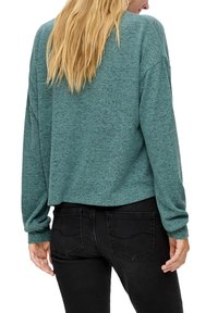 Miętowozielony, krótki sweter z długimi rękawami, o miękkiej fakturze i subtelnym melanżowym wzorze. W połączeniu z dopasowanymi czarnymi dżinsami.