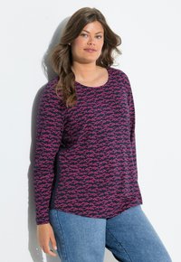 Pitkähihaista violettia toppia, jossa on vaaleanpunainen kalakuvio, pyöreä kaula-aukko ja rento istuvuus. Yhdistetty vaaleansinihin farkkuihin.