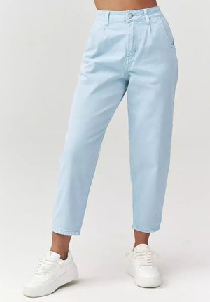 Jasnoniebieskie, wysokowycięte jeansy z prostą nogawką noszone z białymi trampkami, pokazane od talii do stóp na jednolitym tle.