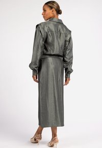 Shiny, dark gray long dress with a collared shirt-style top, padded shoulder accents, and elastic waistband; features puffed sleeves and smooth texture.