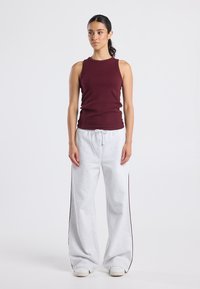 Burgundy sleeveless top paired with light gray wide-leg sweatpants featuring a drawstring and side stripes. Smooth texture, casual design.