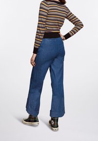Blaue Jeans mit weitem Bein und rohem Saum, kombiniert mit einem mehrfarbigen gestreiften Pullover und karierter High-Top-Sneakern. Lässiges Outfit.