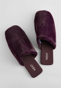 Purple faux fur slippers with a wide, open design, featuring a flat brown sole and embossed "NEXT" branding on the insole.