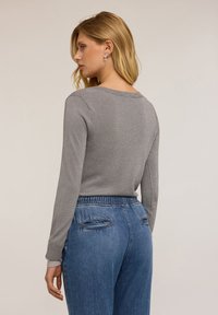 Pulover gri tricotat cu guler rotund, mâneci lungi și o textură strălucitoare; asortat cu pantaloni din denim bleu cu talie înaltă și talie elastică.