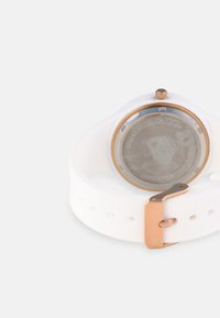 Hvid silikoneur med en rosaguld metalspænde. Rundt sølv rustfrit stål bagside har indgraveret tekst. Enkel design, glat overflade.