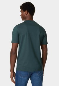 Heren T-shirt met korte mouwen in donkergroen, gemaakt van zacht katoen, heeft een afgeronde halslijn en een relaxte pasvorm, gecombineerd met blauwe spijkerbroeken.