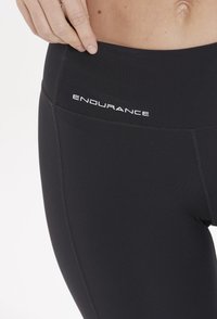 Svarta leggings gjorda av elastiskt material, med en slät yta och resårmidja med "ENDURANCE"-logotypen i vitt.