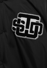 Patch brodé en noir et blanc avec des formes géométriques entrelacées cousues sur un tissu noir.