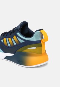 Blå och grön atletisk sko med en texturerad mesh-övre, gula accenter och en gradient orange häl. Har en dragflik för enkel påtagning.