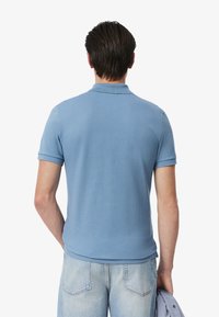 Camisa polo azul claro con acabado texturizado, mangas cortas y cuello de canalé, combinada con jeans de mezclilla claros.