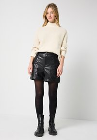 Crème ribbelgebreid trui, zwarte leren shorts met twee knopen, zwarte panty, en dikke zwarte enkelboots.