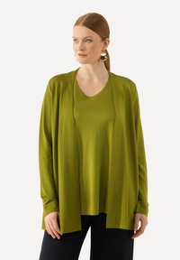 Olivgrüner, leichter Cardigan, über einem passenden T-Shirt getragen, kombiniert mit dunklen Hosen. Glatte Textur, lässiges Design, offenes Vorderteil.