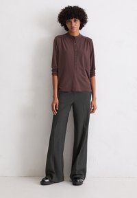 Chemise henley brune à manches longues avec un col et cinq boutons, assortie à un pantalon large gris foncé à rayures et des chaussures noires.