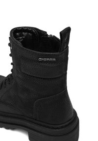 Fekete bőrből készült bokacsizma textúrázott felülettel, fűzős elejével, párnázott nyakrészes kialakítással és hangsúlyos logóval. Vastag talpú és megerősített sarkú.