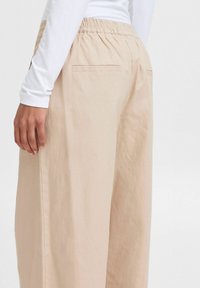 Pantaloni beige chiaro con un design a gamba larga, vita elastica e due tasche posteriori. Realizzati in un tessuto morbido e testurizzato.