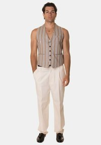 Gilet a righe marroni con scollatura a V, bottoni frontali e tasche laterali, indossato con pantaloni color crema e scarpe nere. Tessuto dalla texture liscia.