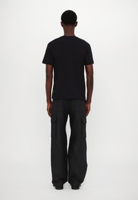 Camiseta negra de cuello redondo y pantalones cargo de pierna ancha. Los pantalones cargo cuentan con bolsillos laterales. Textura suave con un ajuste relajado.